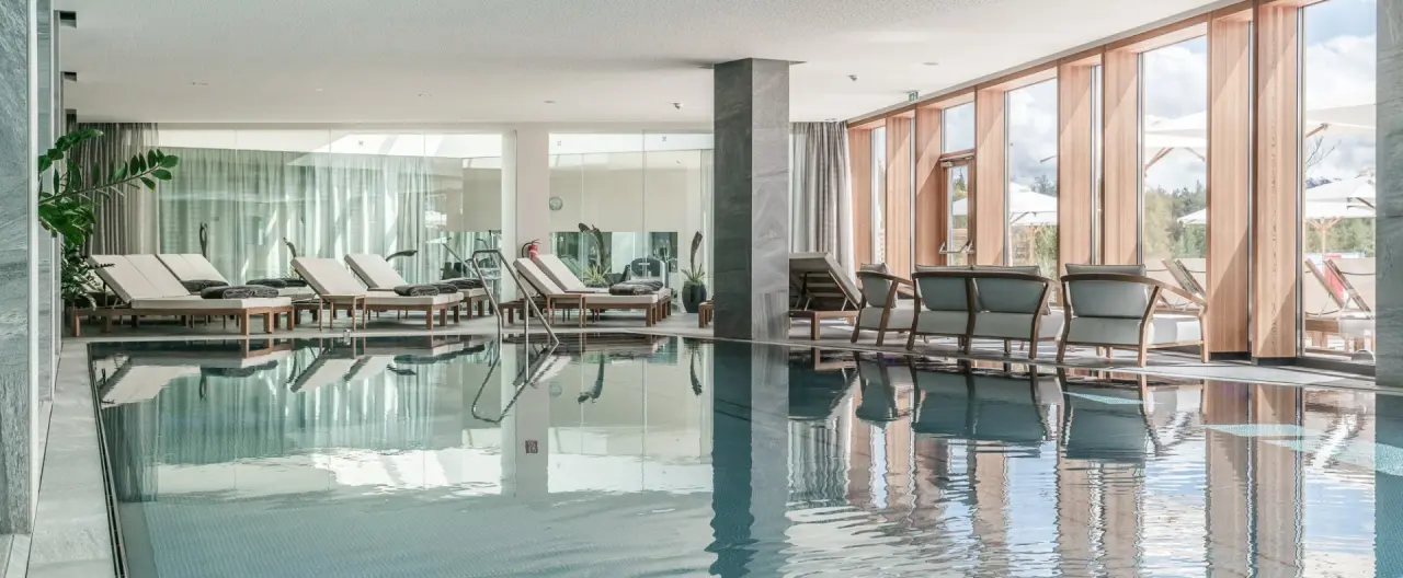 Moderner Innenpool mit Liegebereich und großen Fenstern zum Garten im Hotel Nidum.