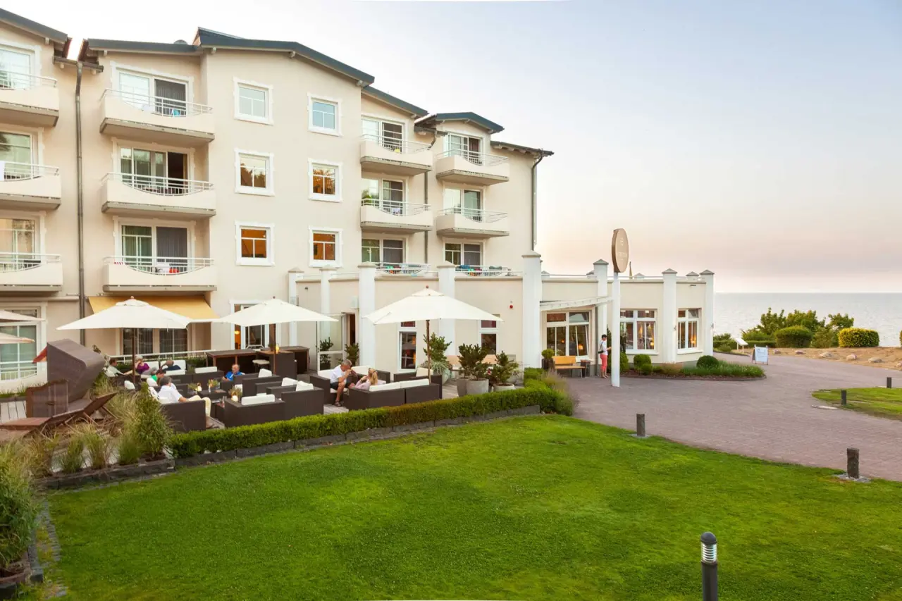 Aussenansicht des Hotel Bernstein mit Terrasse, Gästen und Meerblick auf die Ostsee am Abend.