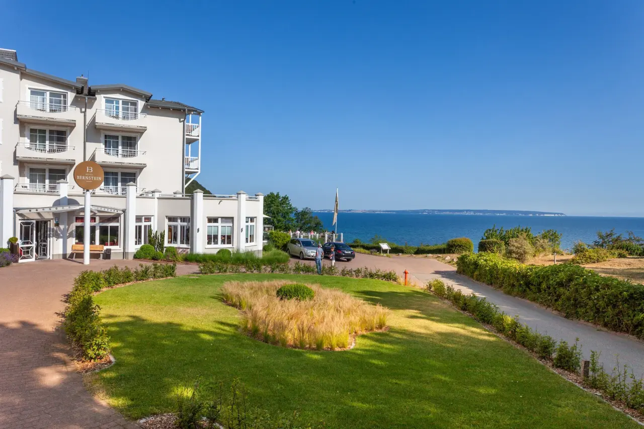 Elegante Aussenansicht des Hotel Bernstein mit gepflegtem Garten und weitem Blick auf die Ostsee unter blauem Himmel.