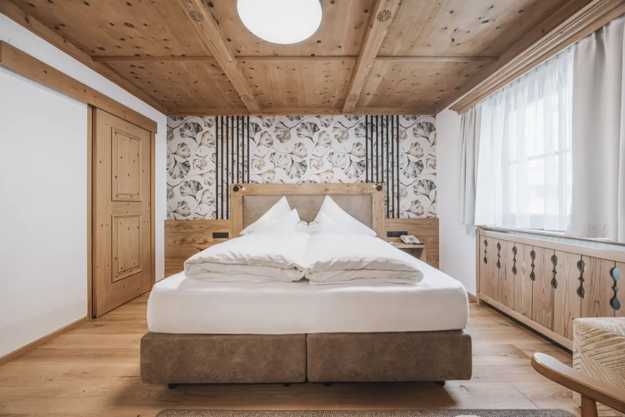 Gemütliches Doppelzimmer im alpinen Stil mit Holzbalkendecke und floraler Tapete im Hotel Gaspingerhof.