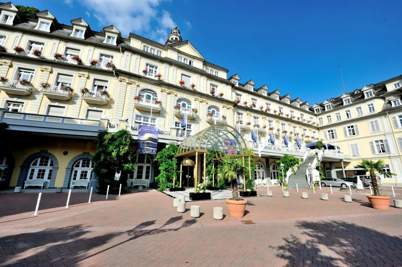 Prächtige Aussenansicht des historischen Häcker´s Grand Hotel Bad Ems mit gelber Fassade, Balkonen und Glas-Eingangsbereich unter blauem Himmel.