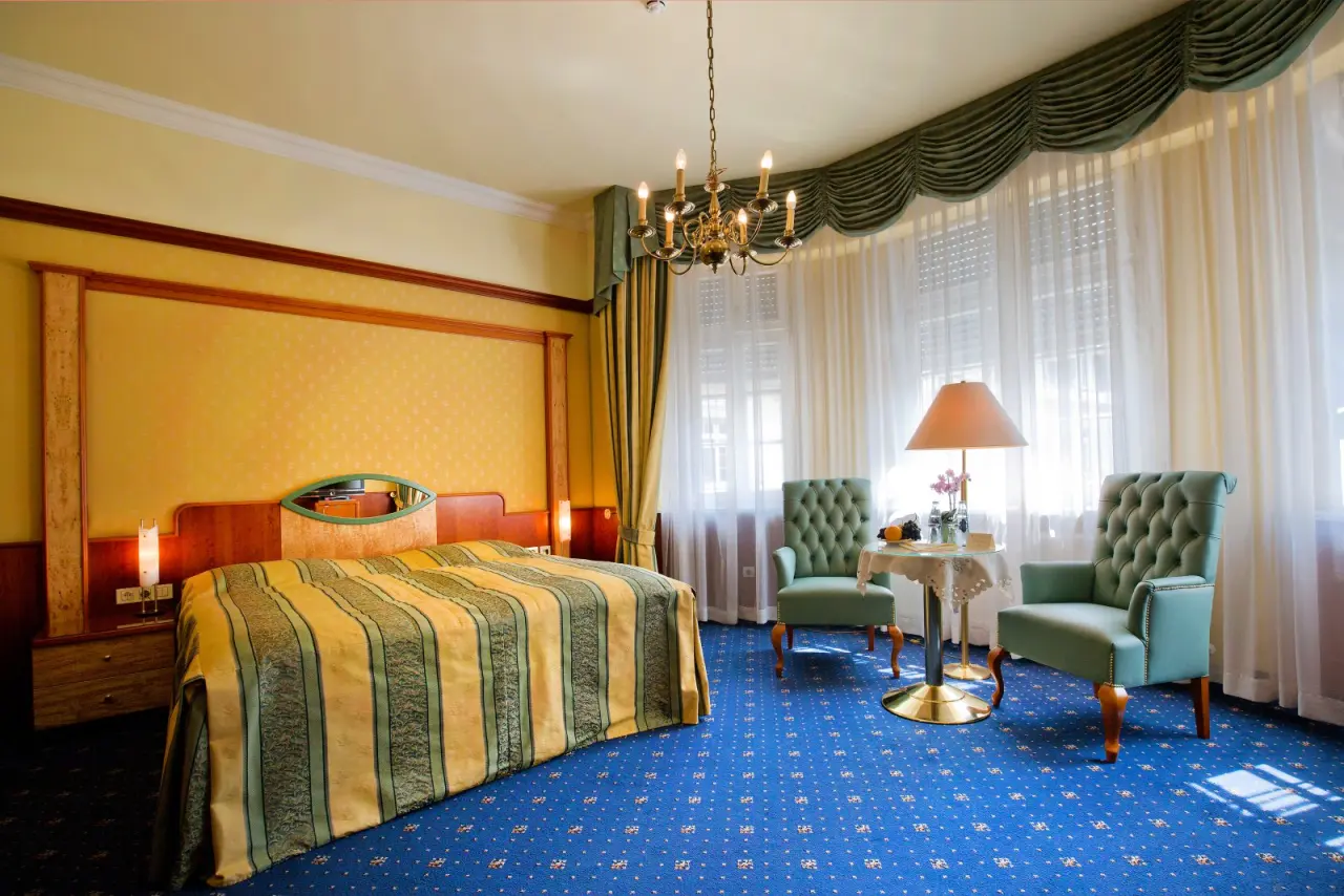 Klassisch eingerichtetes Hotelzimmer im Häcker´s Grand Hotel Bad Ems mit Doppelbett, Sitzbereich und eleganten Vorhängen.