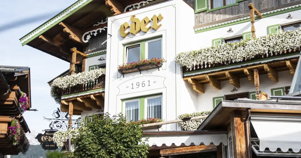 Traditionelle Fassade des Lifestyle-Hotel Eder mit Holzbalkonen, grünen Fensterläden und üppigem Blumenschmuck.