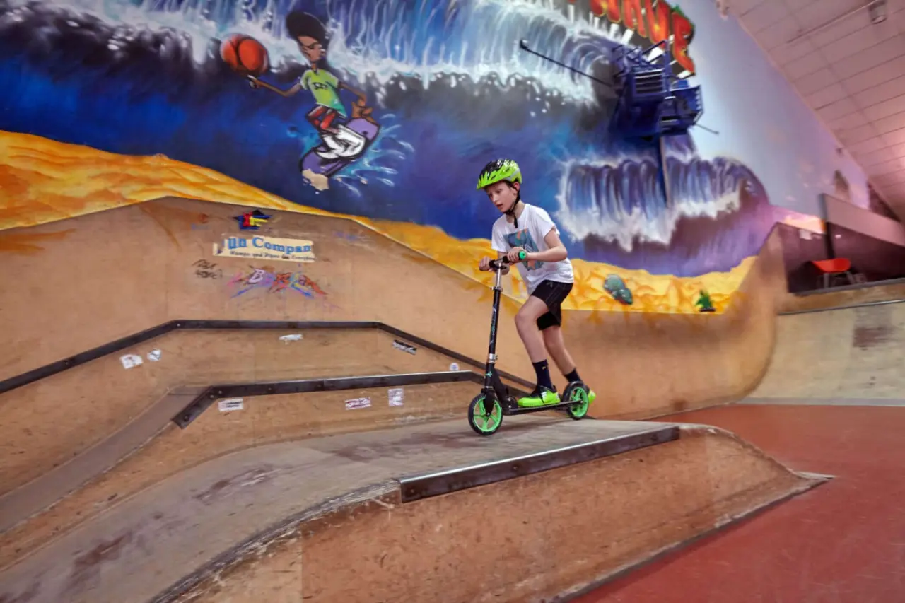 Kind auf Roller in der Indoor-Skatehalle des Ostseehotel Midgard in Dampland. Buntes Wandgemälde im Hintergrund.