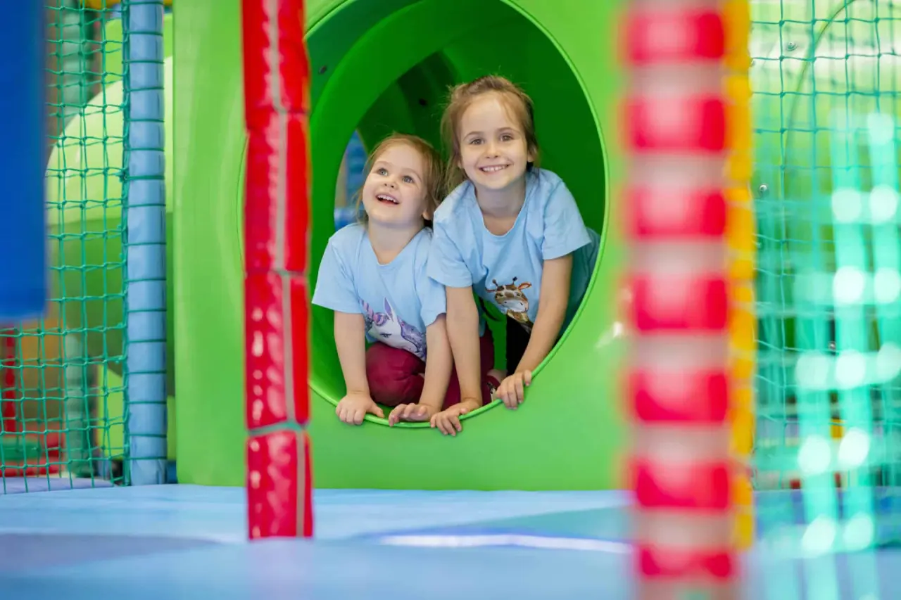 Zwei lachende Kinder in einem bunten Spieltunnel im Kids Club des Ostseehotel Midgard in Dampland.