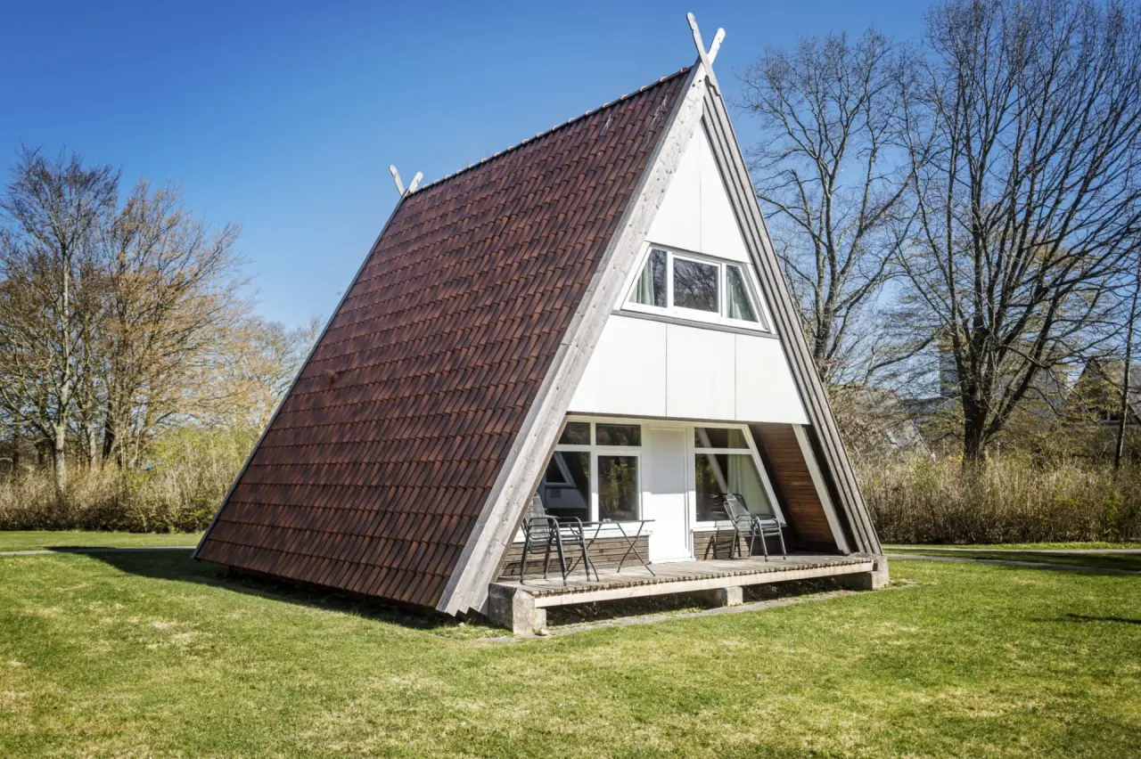 Modernes A-Frame Ferienhaus des Ostseehotel Midgard in Dampland mit Terrasse und grünem Garten unter blauem Himmel.