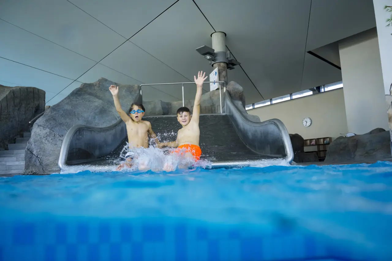 Zwei Kinder rutschen lachend die Wasserrutsche hinunter in den Pool des Ostseehotel Midgard in Dampland.