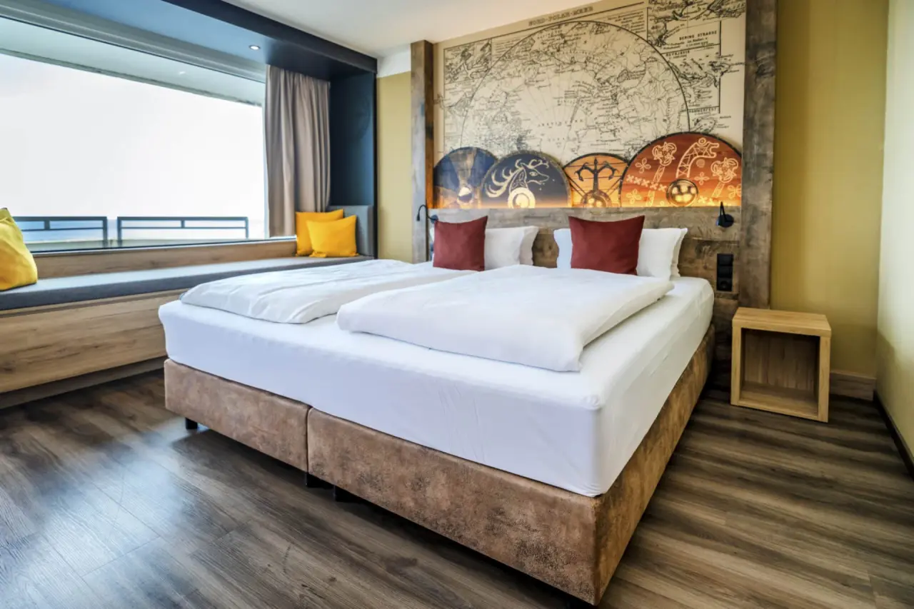 Geräumiges Doppelzimmer im Ostseehotel Midgard mit großem Fenster, gemütlicher Sitzecke und maritimem Design.
