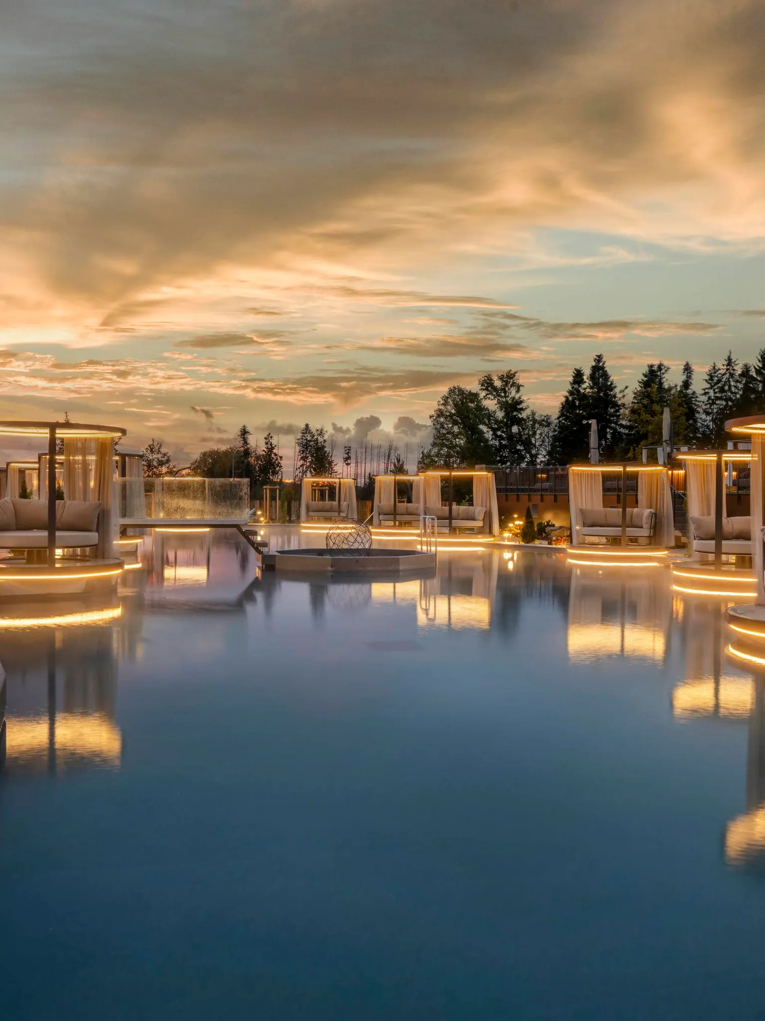 Das Stemp****S Wellnessresort in Büchlberg – Außenpoolbereich mit beleuchteten Daybeds bei Sonnenuntergang | Wellnesshotel Bayerischer Wald