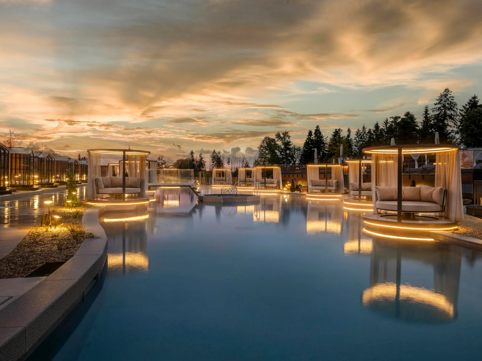 Das Stemp****S Wellnessresort in Büchlberg – Außenpoolbereich mit beleuchteten Daybeds bei Sonnenuntergang | Wellnesshotel Bayerischer Wald