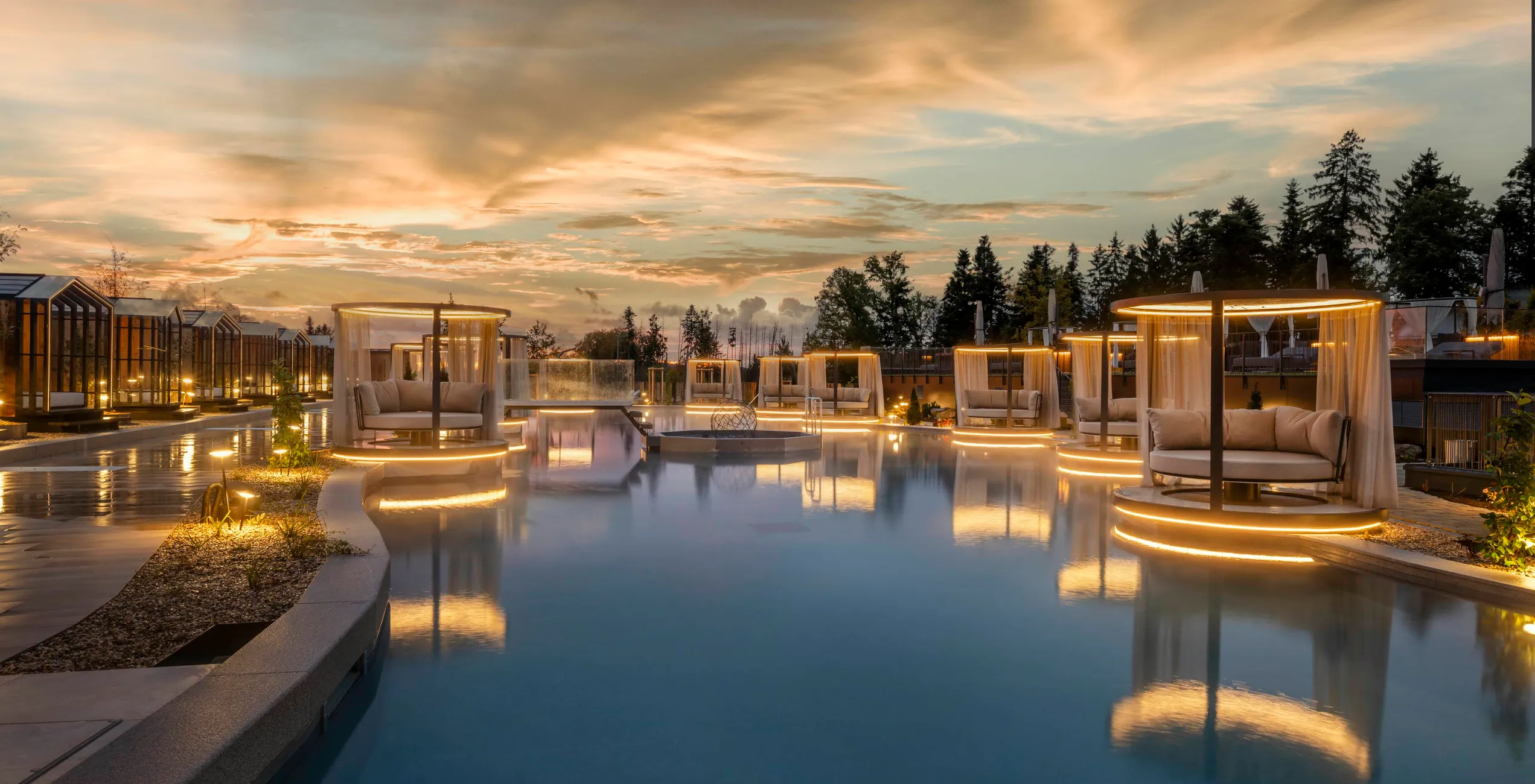 Das Stemp****S Wellnessresort in Büchlberg – Außenpoolbereich mit beleuchteten Daybeds bei Sonnenuntergang | Wellnesshotel Bayerischer Wald