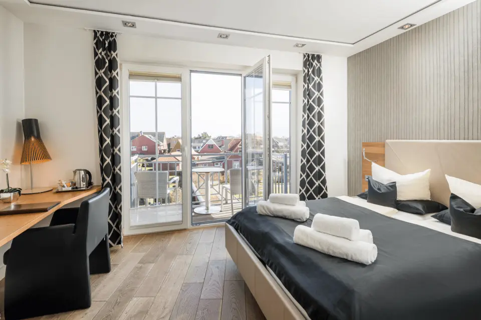 Modernes Hotelzimmer mit Doppelbett, Schreibtisch und Balkonblick im Logierhus Langeoog.