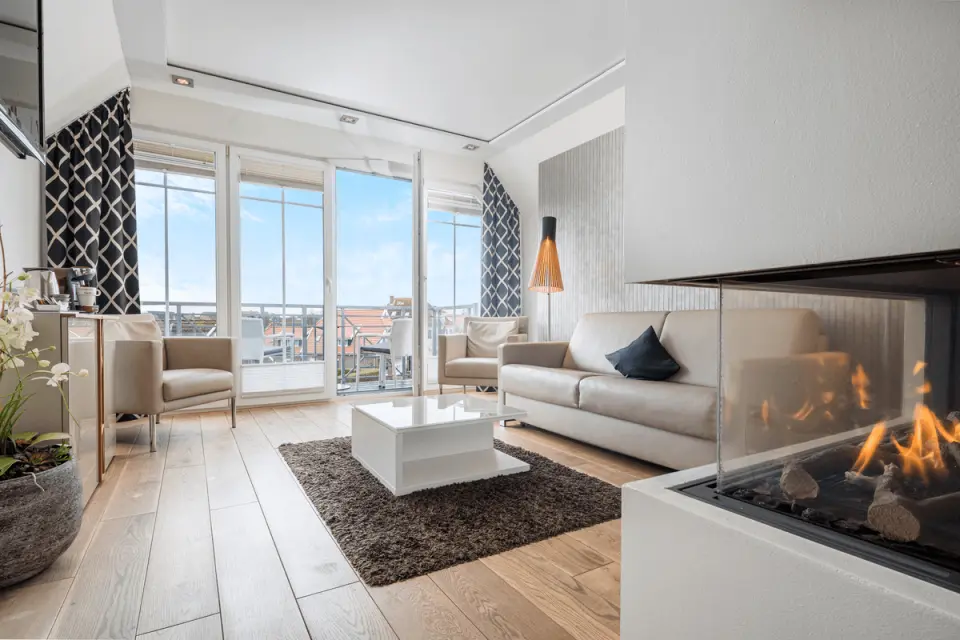 Gemütliches Wohnzimmer einer Suite im Logierhus Langeoog mit Kamin, Sofa und Balkonblick.