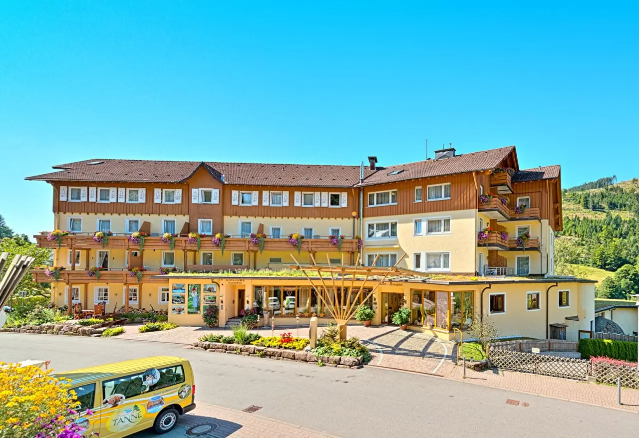 Aussenansicht des Wellness Hotel Tanne Tonbach mit blühenden Balkonen und grüner Umgebung unter blauem Himmel.