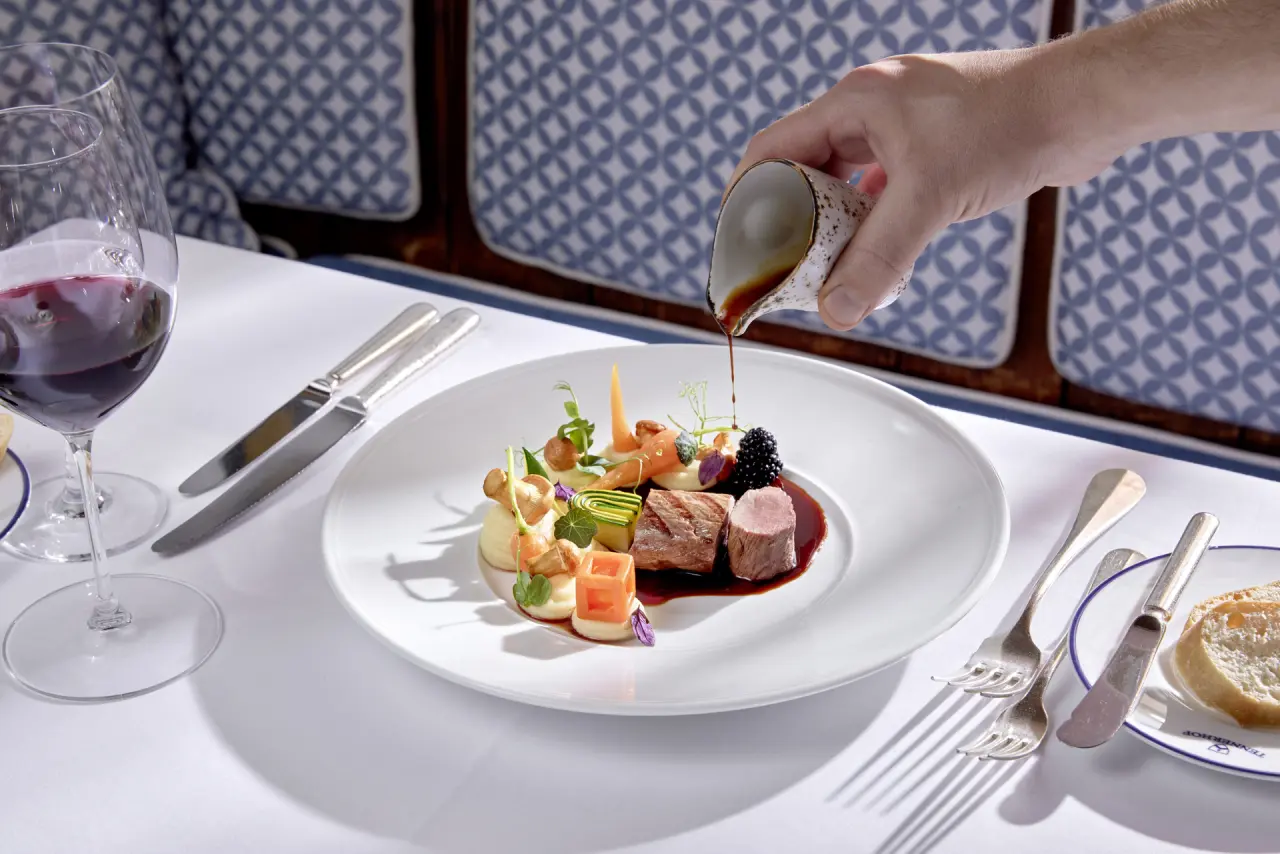 Exquisit angerichtetes Gourmetgericht mit Fleisch und Gemüse, Sauce wird übergossen, im Restaurant des Tennerhof Gourmet & Spa de Charme Hotel.