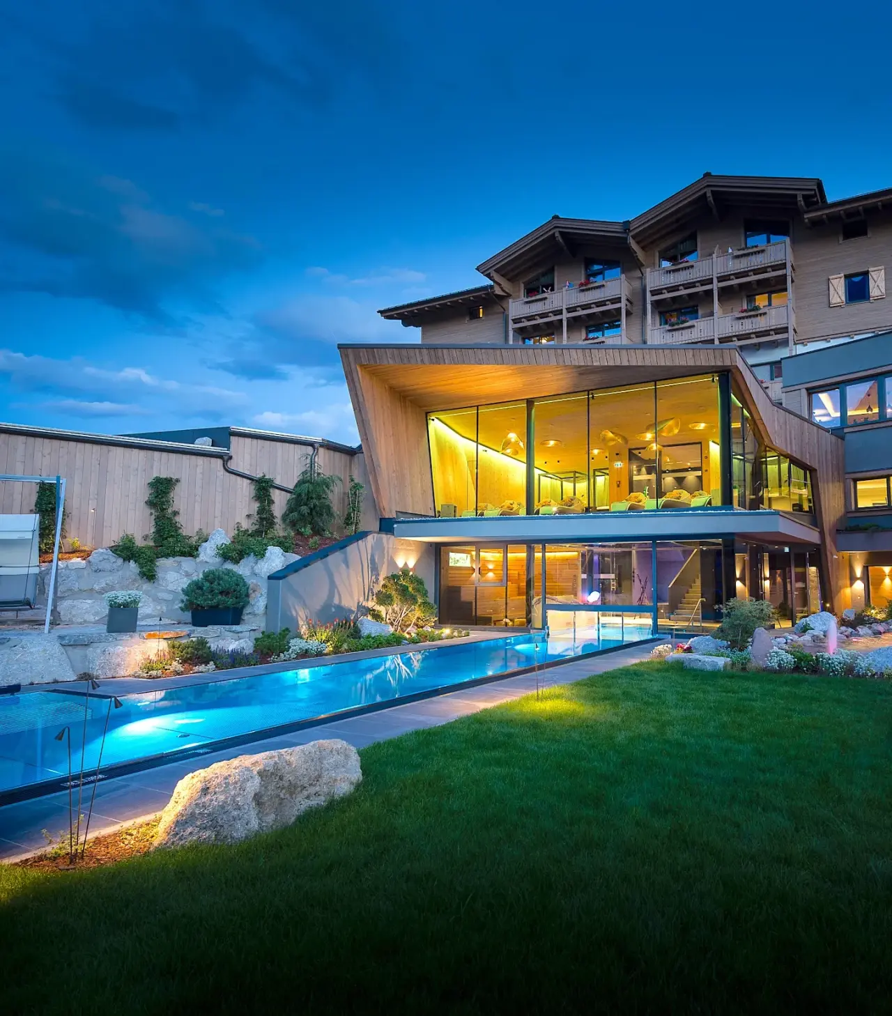 Abendliche Aussenansicht des Good Life Resort Riederalm mit beleuchtetem Aussenpool und modernem Spa-Bereich.