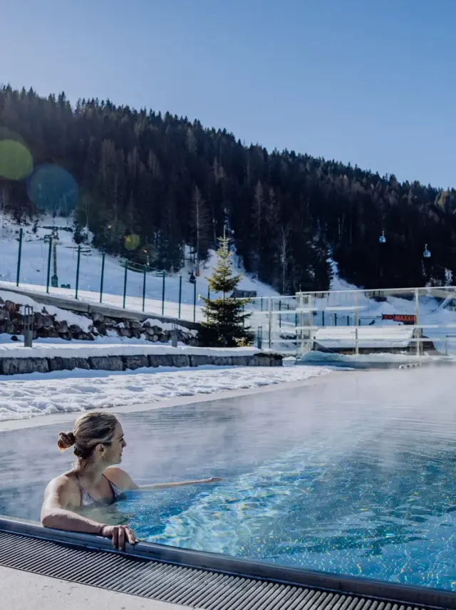 Good Life Resort Riederalm in Leogang – Frau entspannt im beheizten Außenpool im Winter | Wellnesshotel Salzburger Land