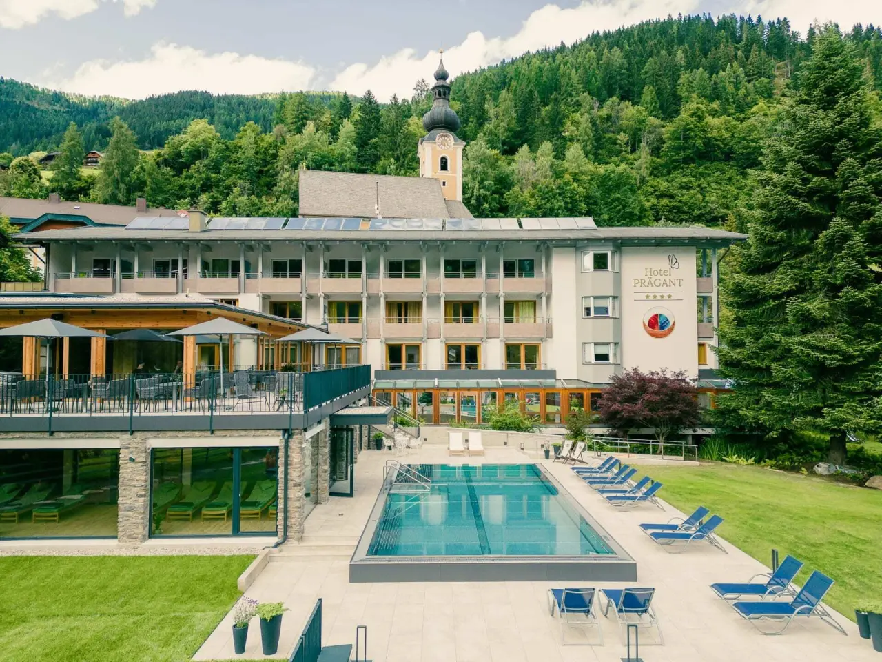 Aussenansicht des Evident Hotel Prägant**** mit grossem Aussenpool, Liegewiese und Bergpanorama.