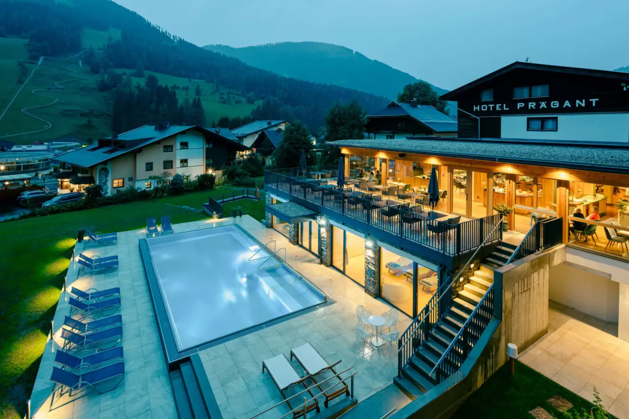 Abendliche Aussenansicht des Evident Hotel Prägant mit beleuchtetem Aussenpool und Bergblick.