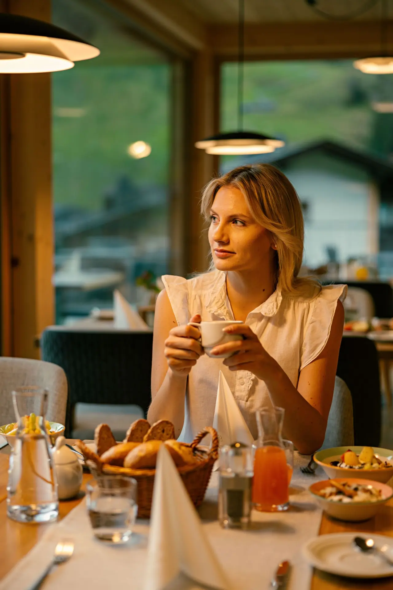 Frau genießt Frühstück mit Kaffee im gemütlichen Restaurant des Evident Hotel Prägant**** mit Blick ins Grüne.