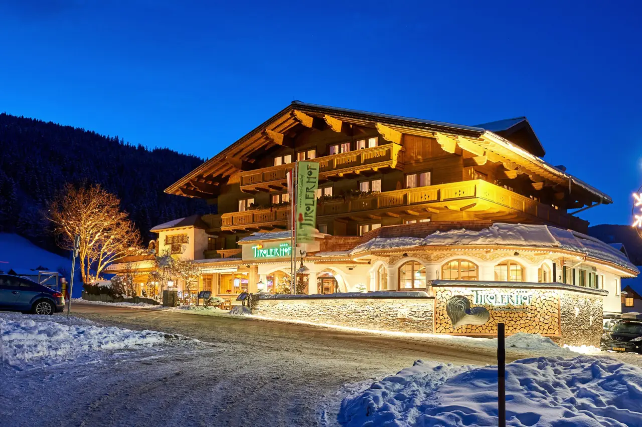 Beleuchtetes Hotel Tirolerhof im traditionellen Alpenstil bei winterlicher Abenddämmerung, umgeben von Schnee und Bergen.