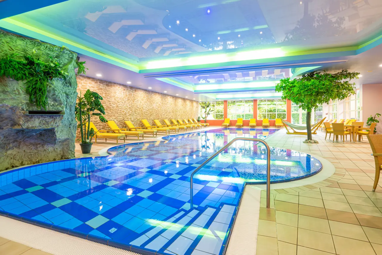Grosszügiger Innenpool im Hotel Schmelmer Hof mit bequemen Liegen, Felswand-Dekor und bunten Lichtern für entspannte Stunden.