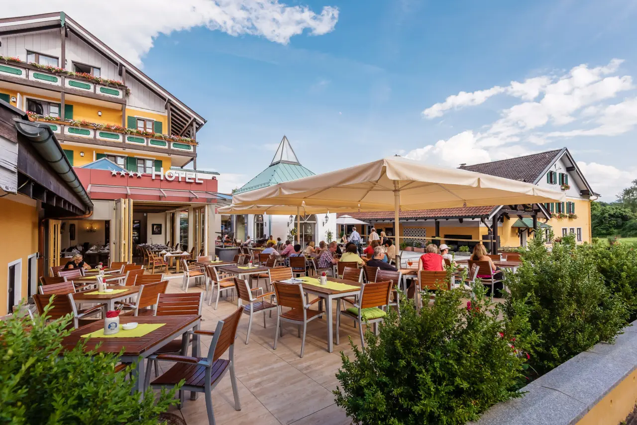 Sonnige Restaurant-Terrasse des Hotel Schmelmer Hof mit Gästen und traditioneller Architektur im bayerischen Stil.