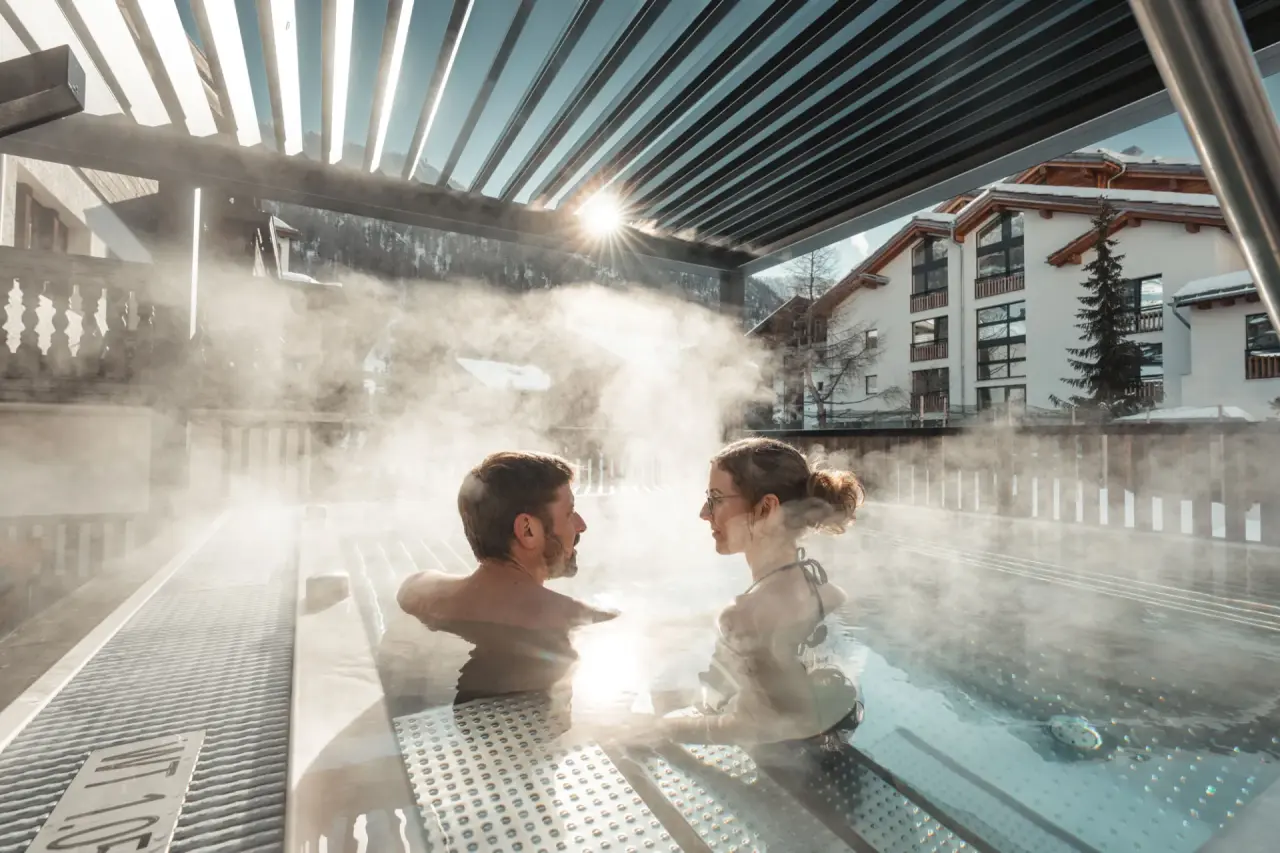 Paar entspannt im dampfenden Outdoor-Whirlpool des Alpen Resort Hotel mit Bergblick im Winter.