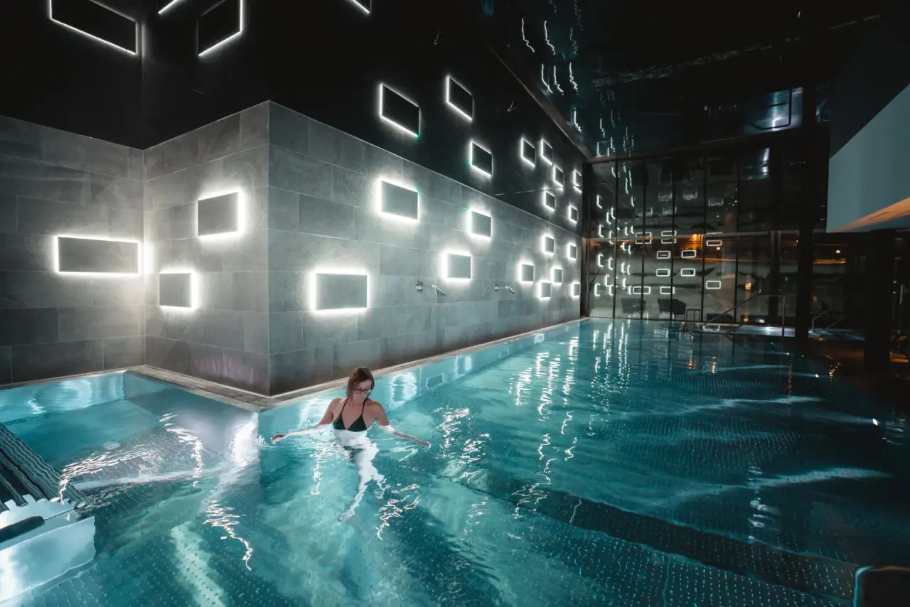 Modernes Hallenbad im Alpen Resort Hotel mit stilvoller Beleuchtung und einer Person, die im Wasser entspannt.
