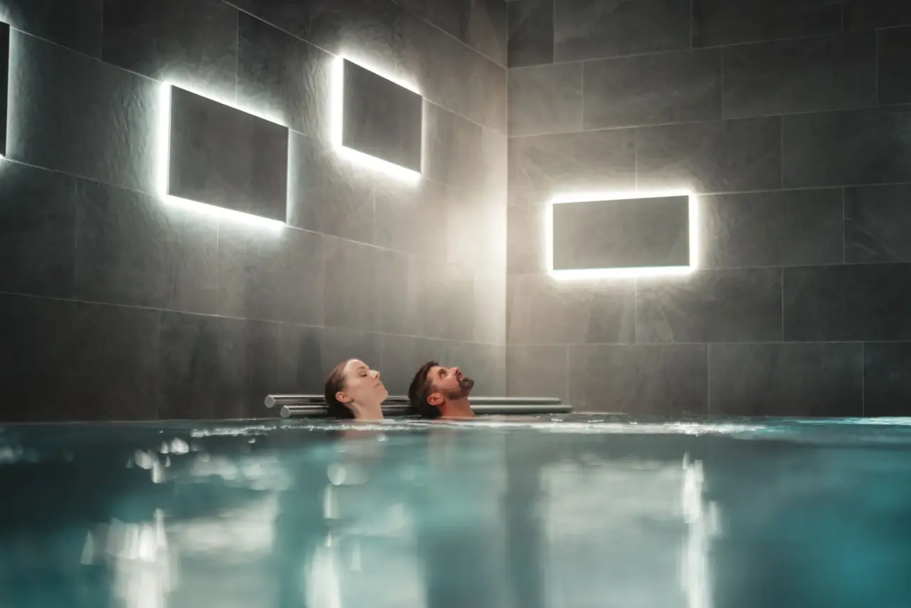 Paar entspannt im modernen Poolbereich mit indirekter Beleuchtung im Alpen Resort Hotel.
