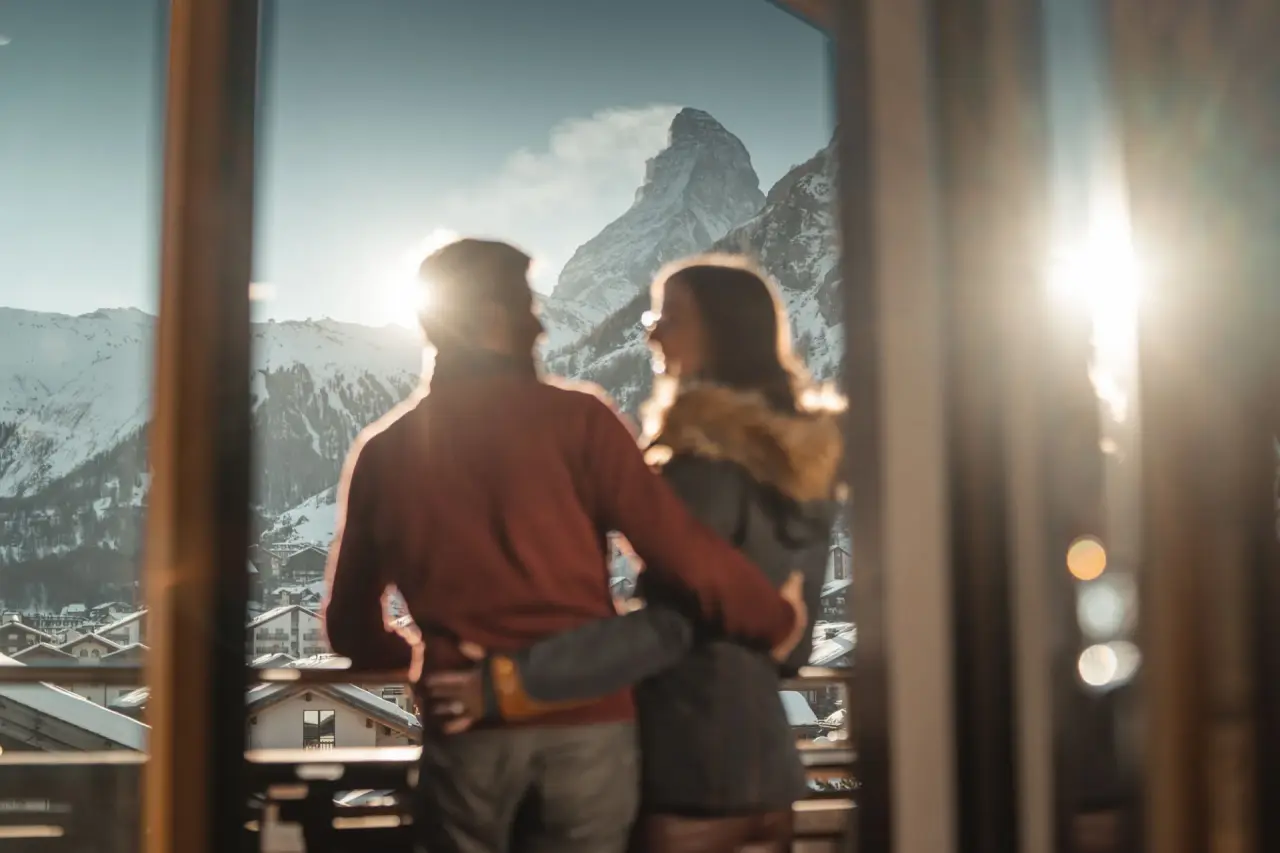 Romantisches Paar genießt den atemberaubenden Blick auf das Matterhorn und die verschneite Alpenlandschaft vom Balkon des Alpen Resort Hotel.