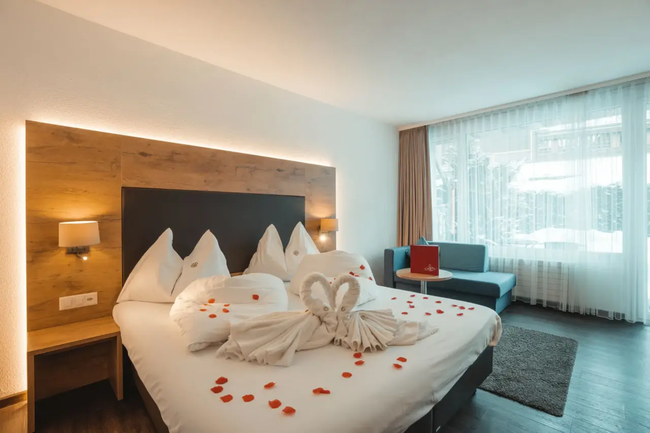 Romantisch dekoriertes Doppelzimmer mit Holzelementen und Blick auf verschneite Bäume im Alpen Resort Hotel.