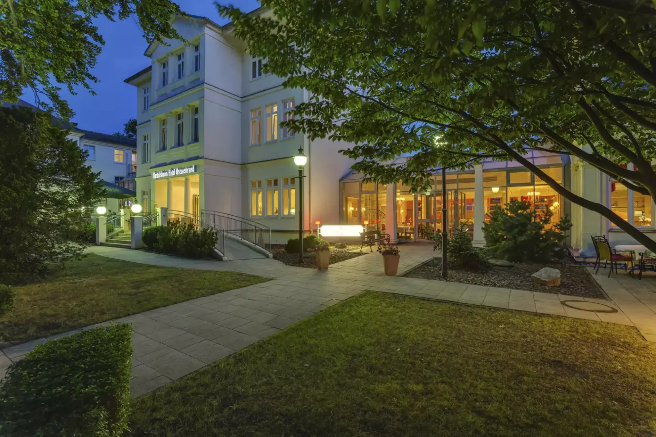 Abendliche Aussenansicht des Upstalsboom Hotel Ostseestrand mit beleuchtetem Eingang und Terrasse.