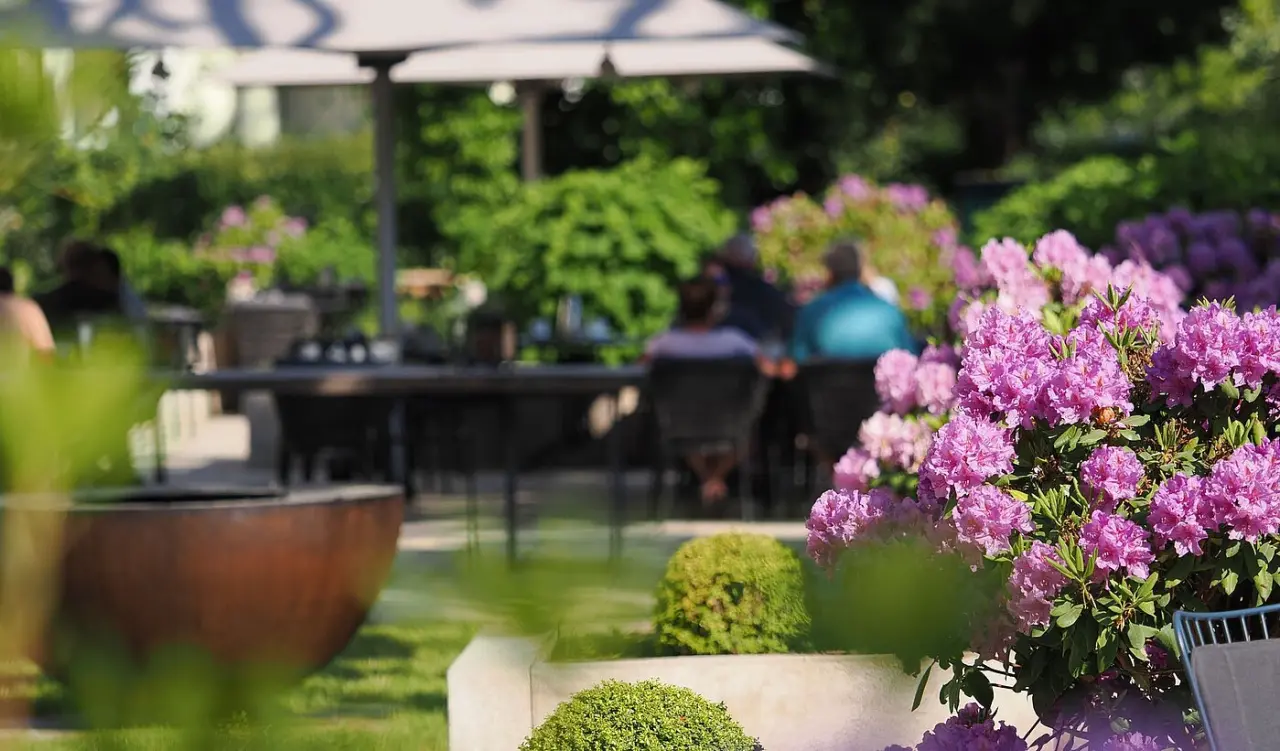 Blühende Rhododendren im Gartenbereich des Upstalsboom Hotel Ostseestrand mit Gästen auf der Terrasse.