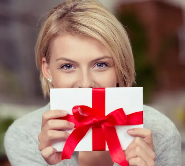 Frau hält einen Geschenkgutschein mit roter Schleife. Ideal für ein Wellness-Erlebnis im Freund Das Hotel & Natur Resort.