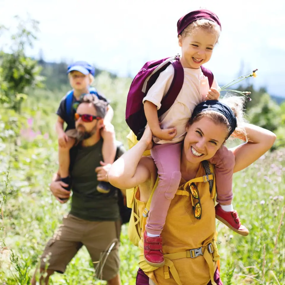 Glückliche Familie wandert mit Kindern auf den Schultern durch die grüne Natur des Freund Das Hotel & Natur Resort.