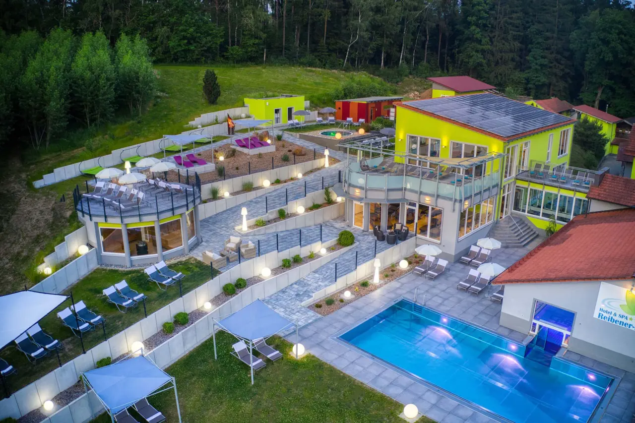 Luftbild des Hotel & SPA Reibener-Hof mit Aussenpool, Sonnenterrassen und modernen Gebäuden inmitten grüner Natur.