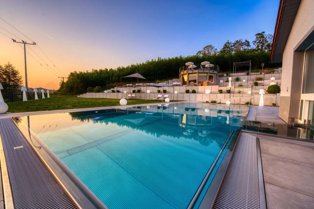 Aussenpool bei Sonnenuntergang mit beleuchteter Terrasse und Gartenanlage im Hotel & SPA Reibener-Hof.