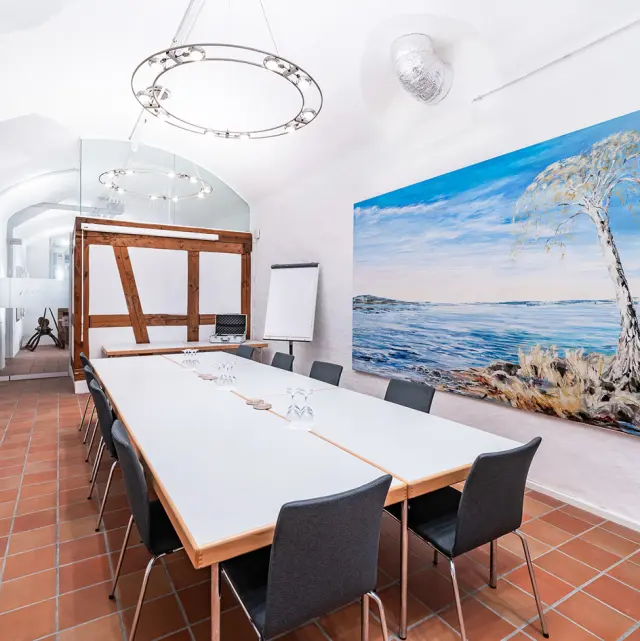Tagungsraum im BLUME. Baden Hotel & Restaurant mit großem Tisch, Stühlen und Flipchart, dekoriert mit einem Landschaftsgemälde.