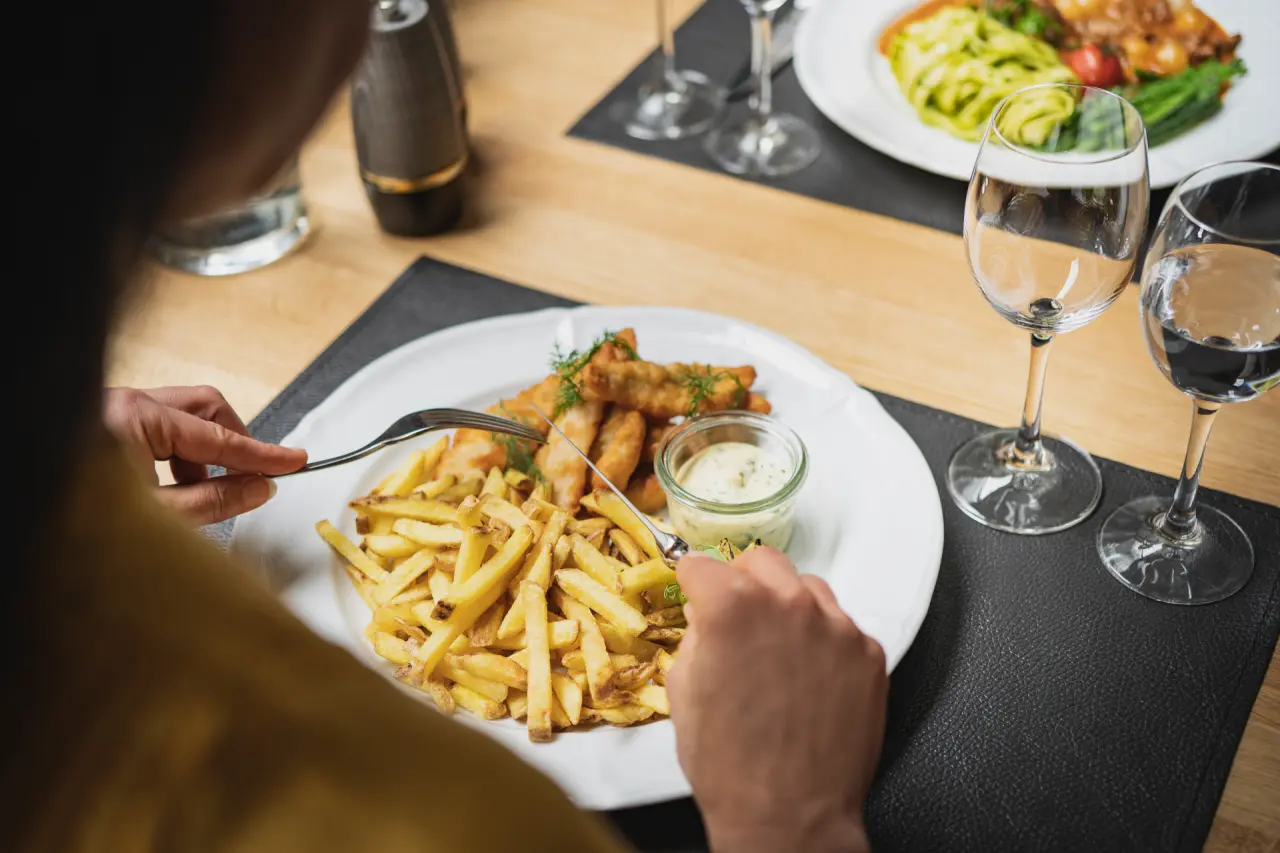 Gast genießt Fish and Chips mit Pommes und Sauce im Restaurant des BLUME. Baden Hotel.