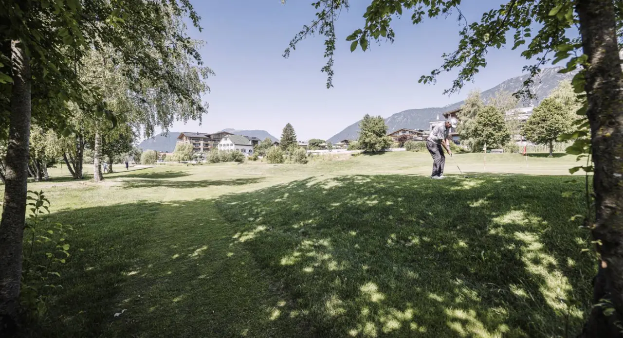 Golfspieler auf dem gruenen Golfplatz des Alpenresort Schwarz mit Bergkulisse im Hintergrund.