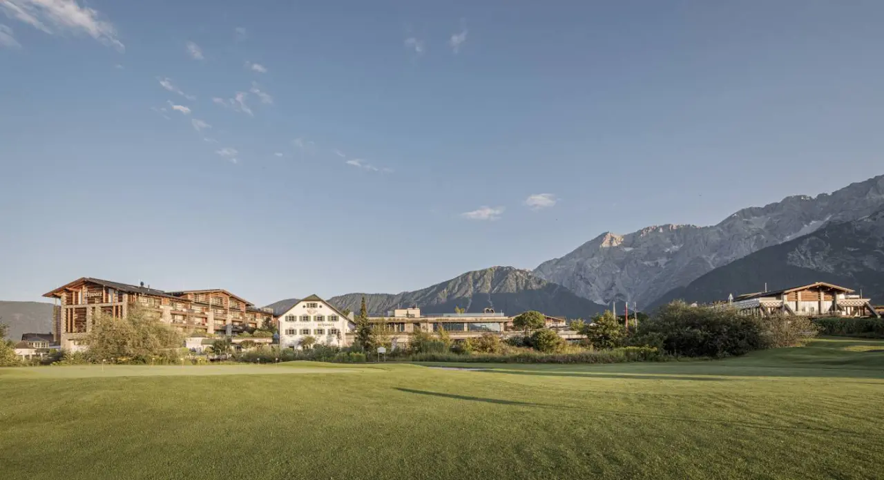 Alpenresort Schwarz mit traditioneller Architektur und Golfplatz vor imposanter Bergkulisse.