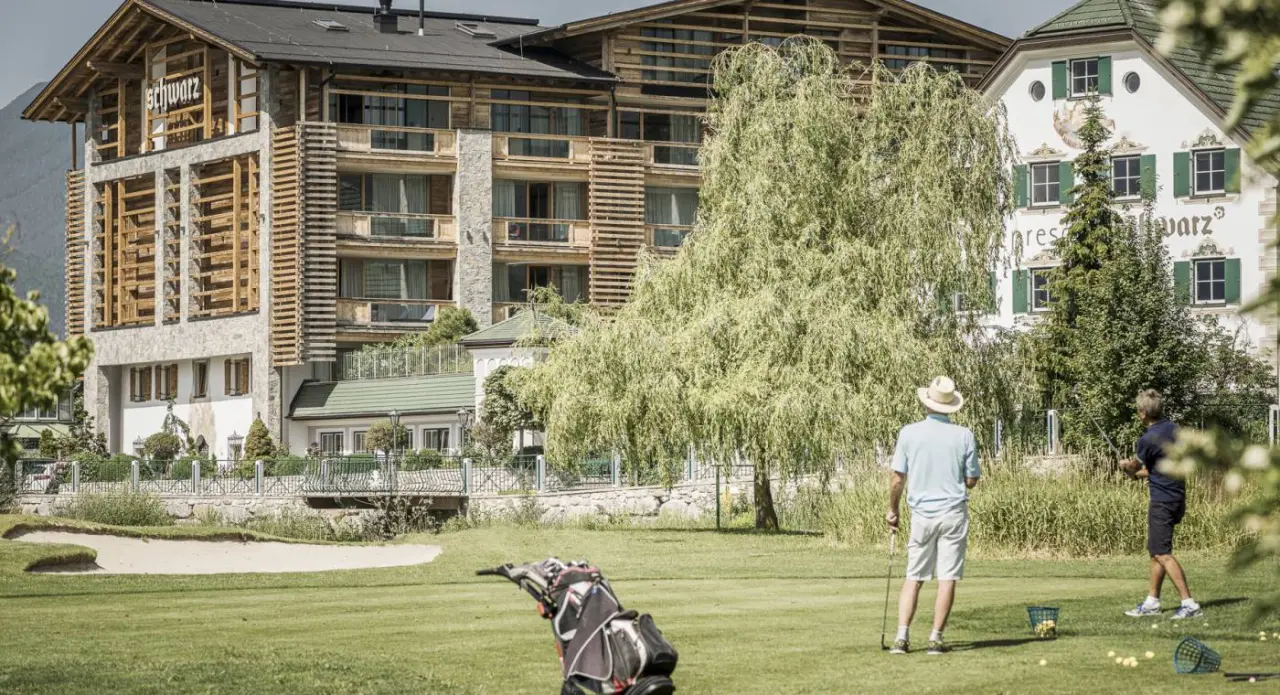 Alpenresort Schwarz mit Golfplatz und Golfern im Vordergrund, umgeben von grüner Natur und Bergen.
