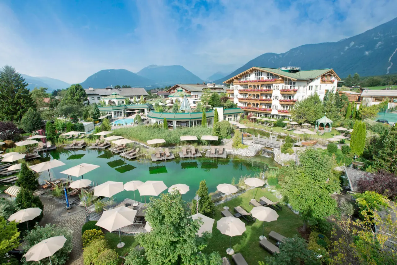 Weitläufige Aussenansicht des Alpenresort Schwarz mit Naturbadeteich, Liegewiesen und Alpenpanorama.