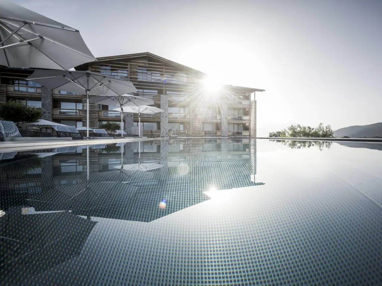 Infinity Pool mit Sonnenstrahlen und Blick auf das moderne Alpenresort Schwarz Hotelgebäude in den Bergen.