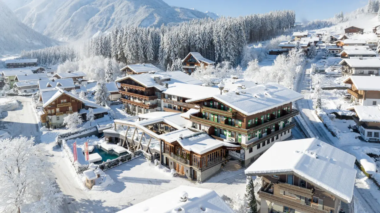 Winterliche Luftaufnahme des Hotel Gassner 4 Sterne Superior mit verschneiten Dächern, Bergen und Wald im Salzburger Land.