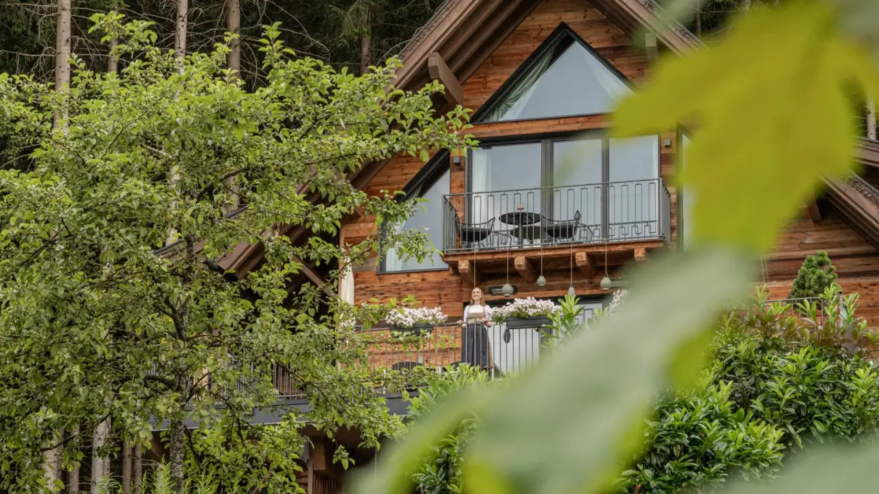 Balkon eines Holzhotels mit blühenden Blumenkästen, umgeben von Bäumen im Hotel Gassner 4 Sterne Superior.