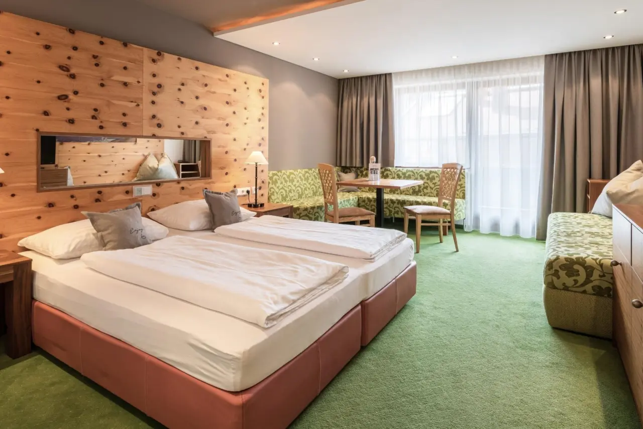 Komfortables Doppelzimmer im Hotel Gassner 4 Sterne Superior mit Holzwand, gemütlichem Sitzbereich und Blick ins Grüne.