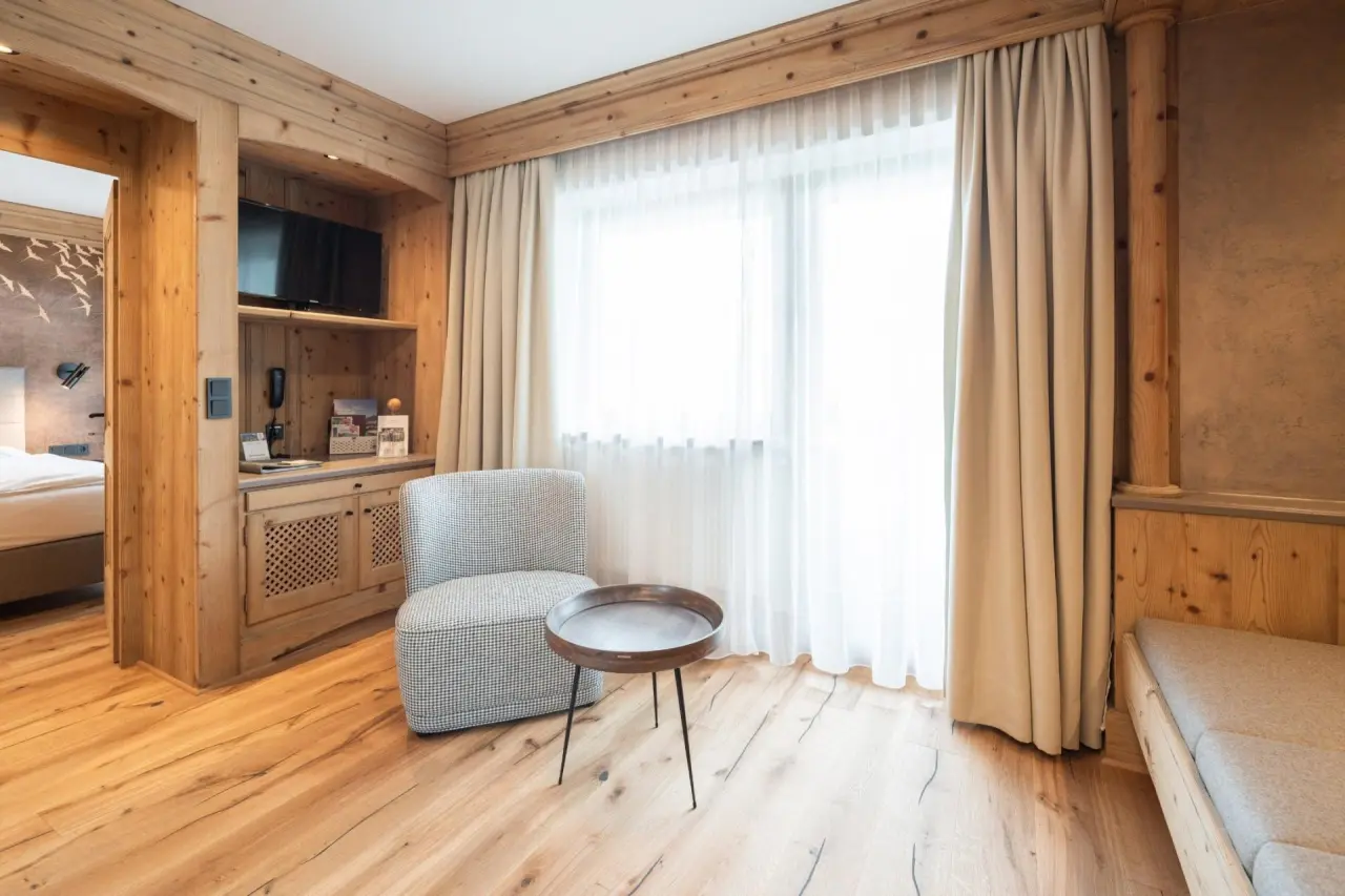 Gemütliches Hotelzimmer im alpinen Stil mit Holzelementen, Sessel und Balkonzugang im Hotel Gassner 4 Sterne Superior.