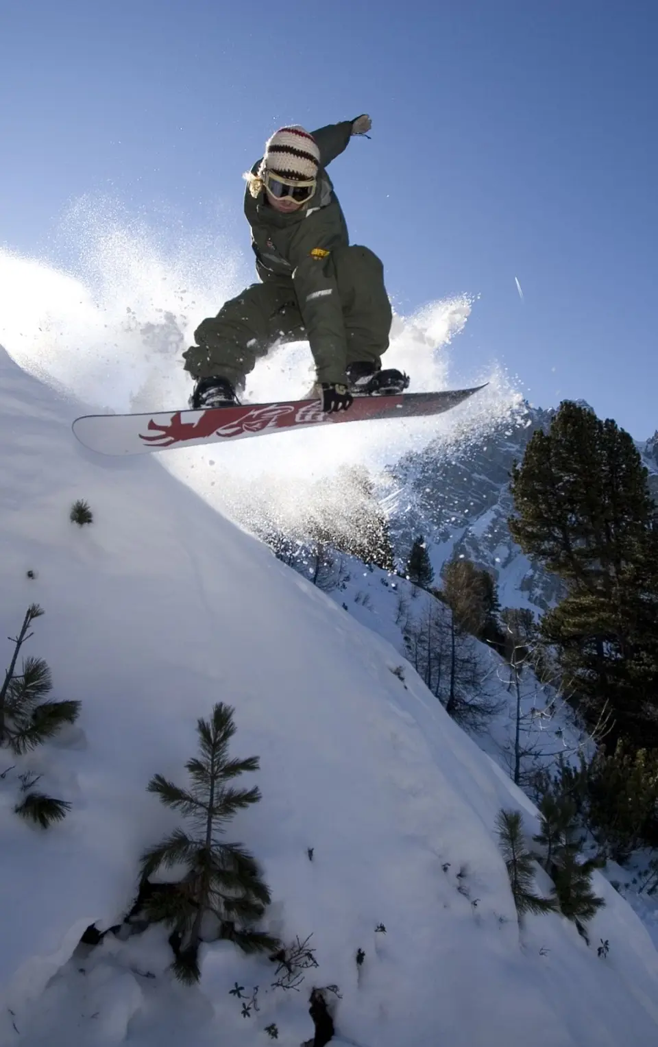 Snowboarder springt im Tiefschnee vor Bergpanorama. Wintersporterlebnis am Sporthotel Cristall in den Alpen.